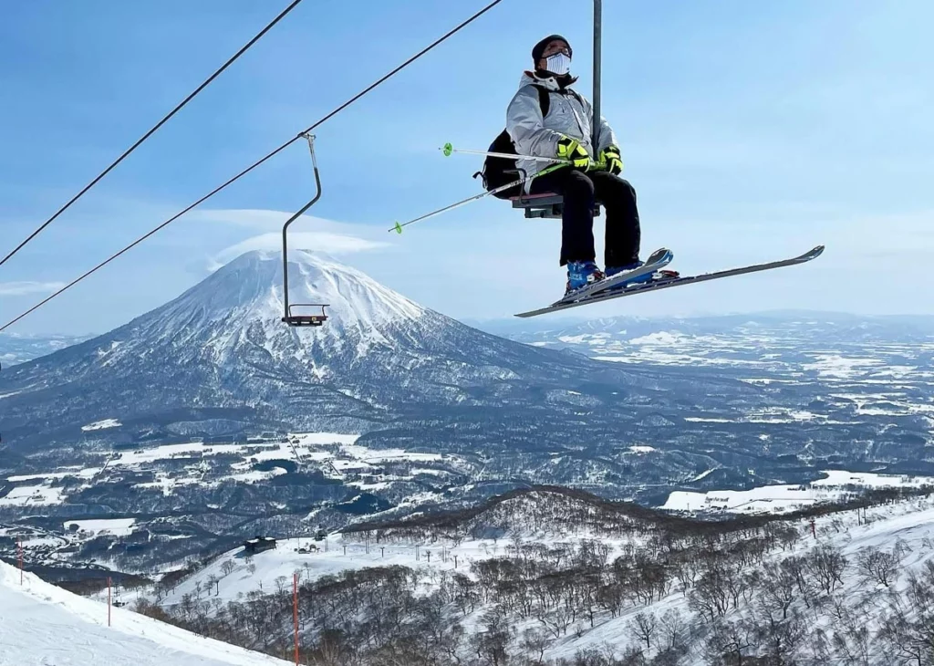 solo rider on the Niseko 'pizza box' chairlift - a single seater with no back or sides, a soft-topped snowy-capped volcano behind in the distance. Contender for world's best ski lift