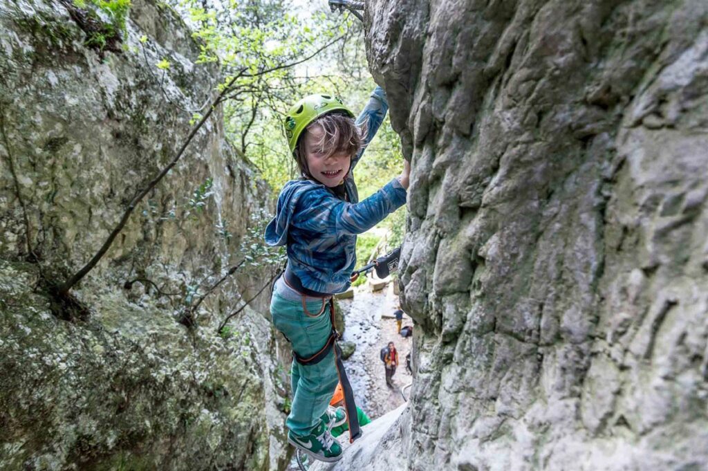 young child smiling and holding onto rock wall mid-climb