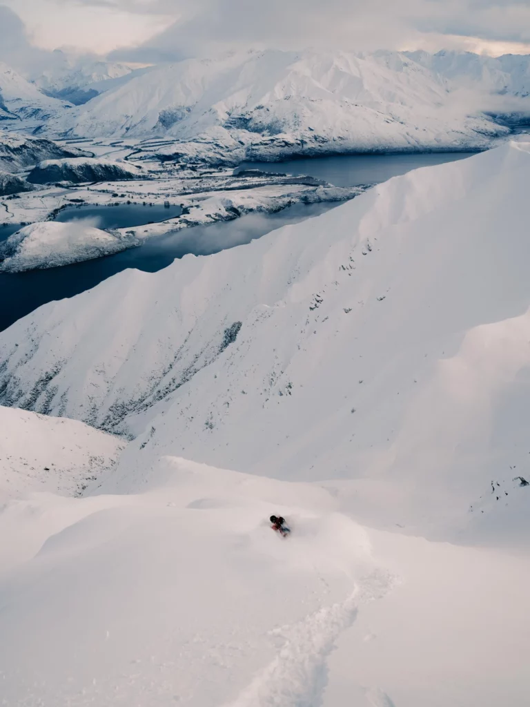 a snowboarder or skier skis fresh, deep snow down a gulley towards a lake