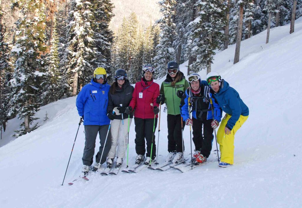 a group of skiers, smiling into camera on the slope, in front of a forest