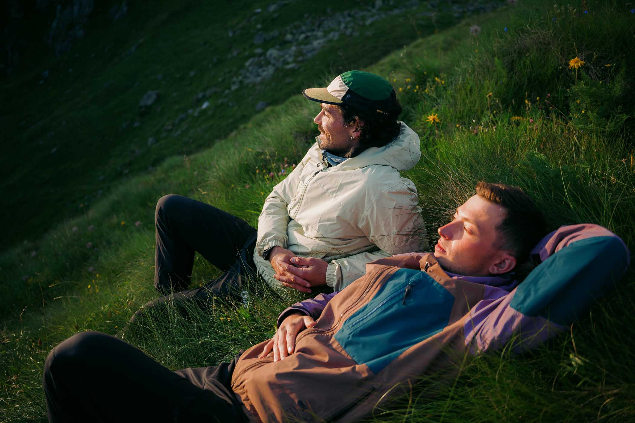 two people lying on long green grass wearing Picture clothing, relaxing, mid hike