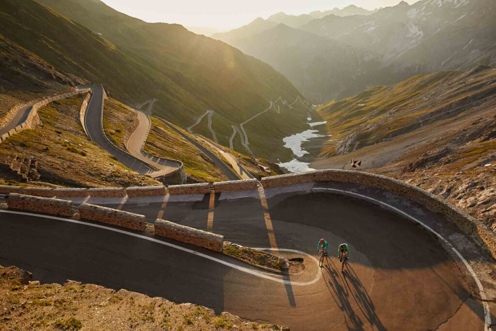 hair pin bends on a alpine road, shot at dusk during golden hour, with a river running through the valley far below