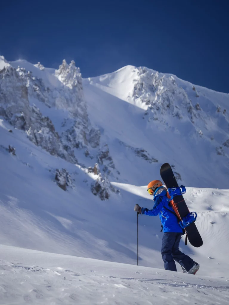 snowboarder-splitboarder hikes uphill under big snowy face