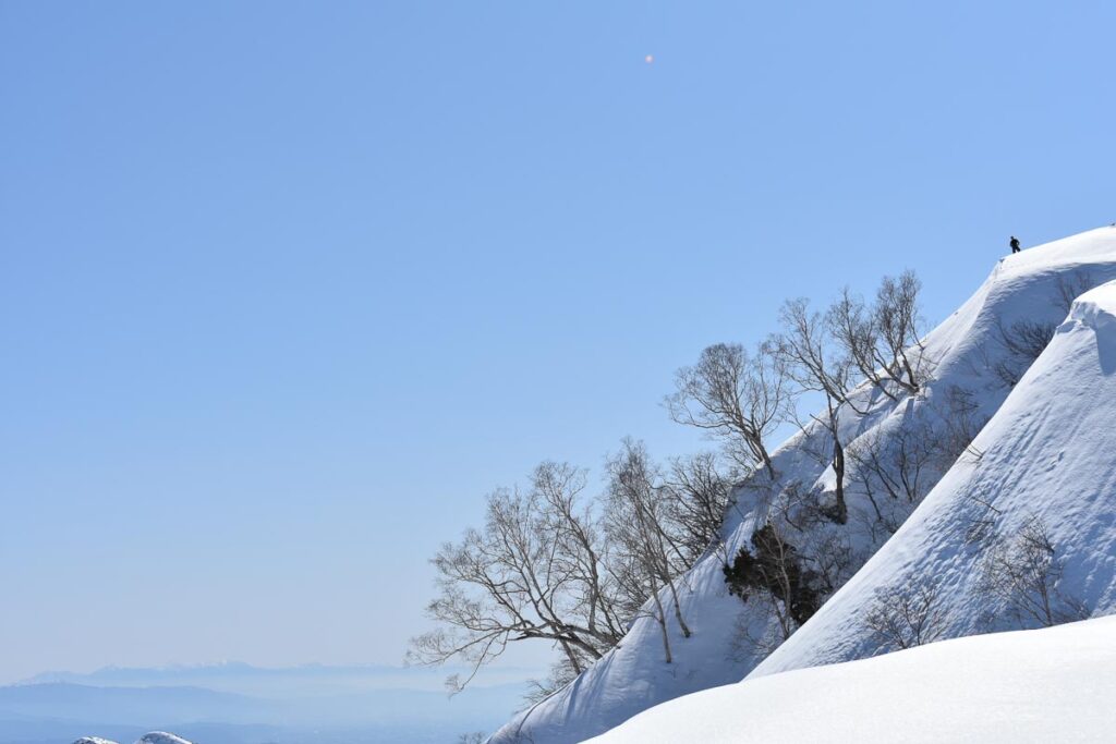 one silhouette looks over the edge of a snowy slope, distant mountains as a backdrop