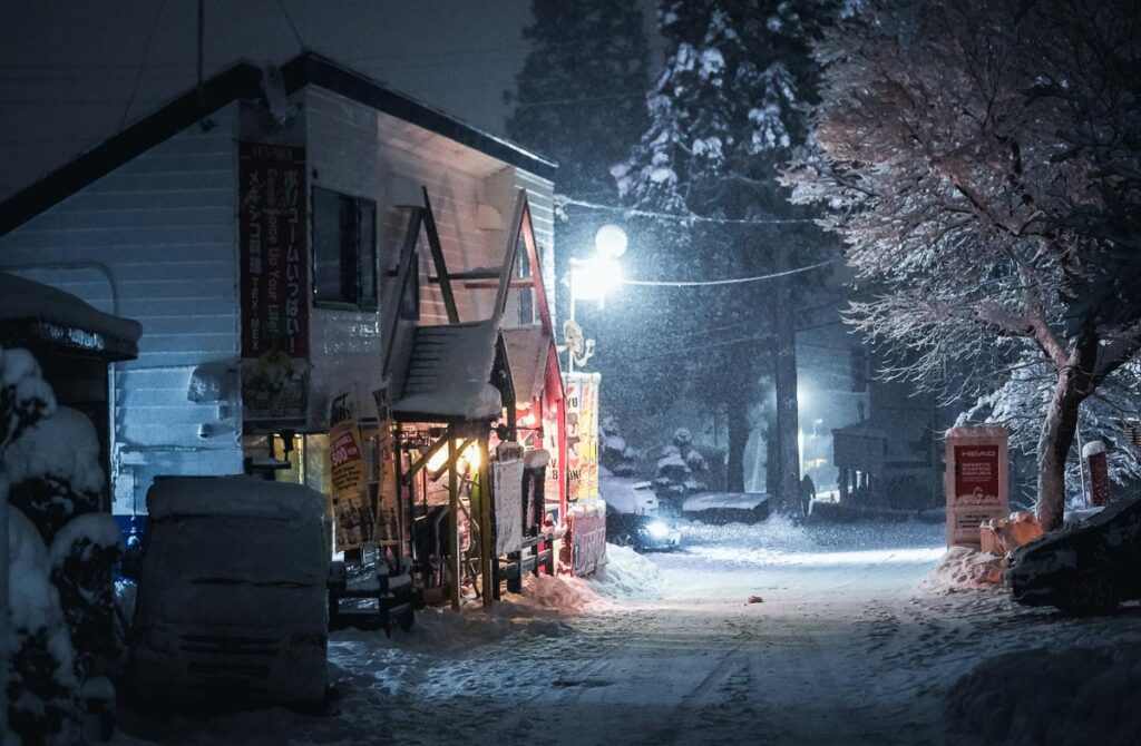 a snowy night with a Japanese restaurant lit up by a streetlight