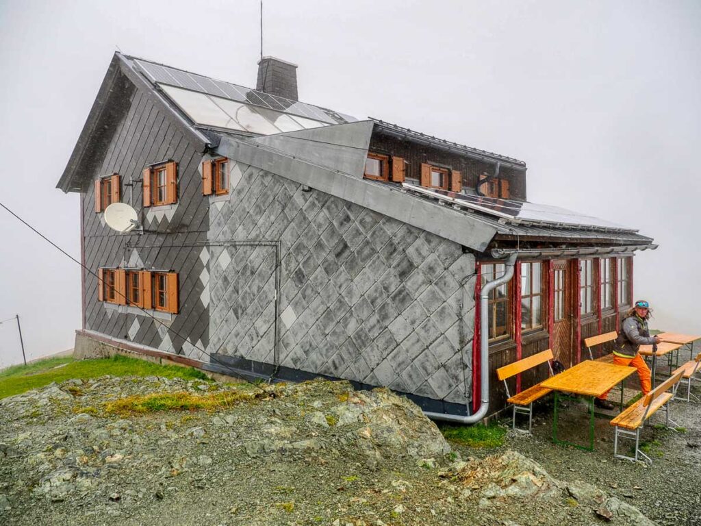 a stone mountain hut, seemingly perched atop a mountain, looks cosy on a cloudy moody day