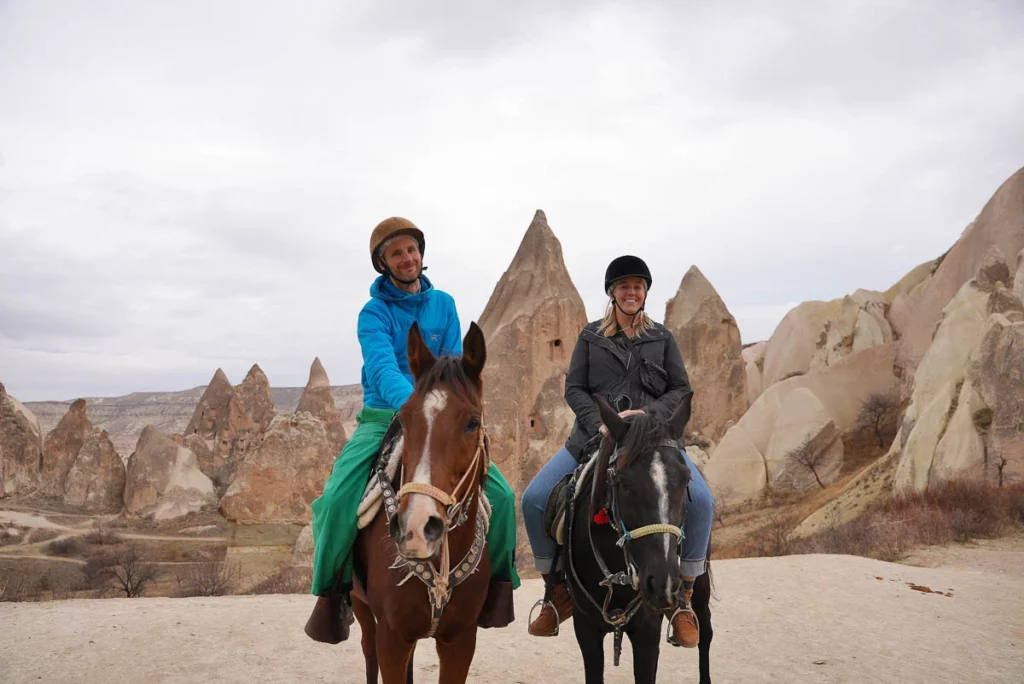 two horse riders smile at camera in front of Cappadocia rock formations in Turkey