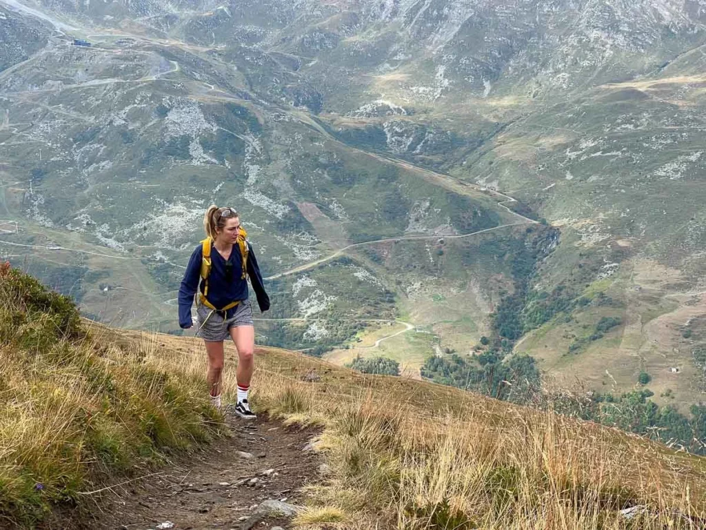 Writer Katie Bamber walking uphill on a route, high above the green-brown valley below