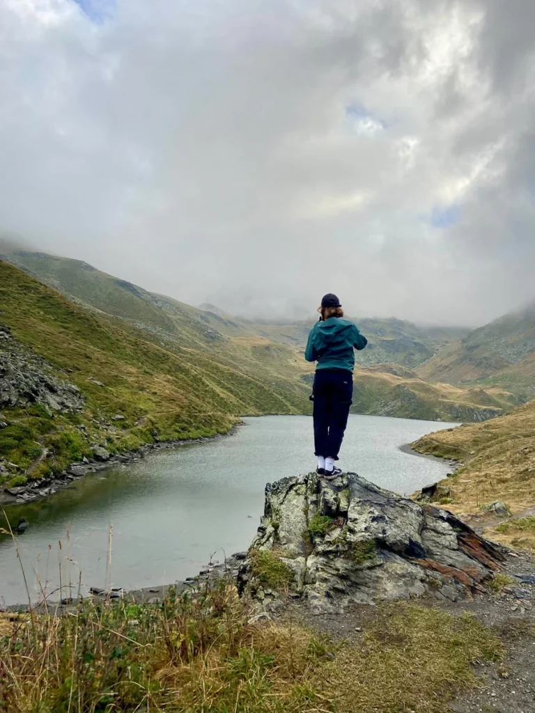 woman stands on a rock, overlooking a lake on a moody day in the high mountains