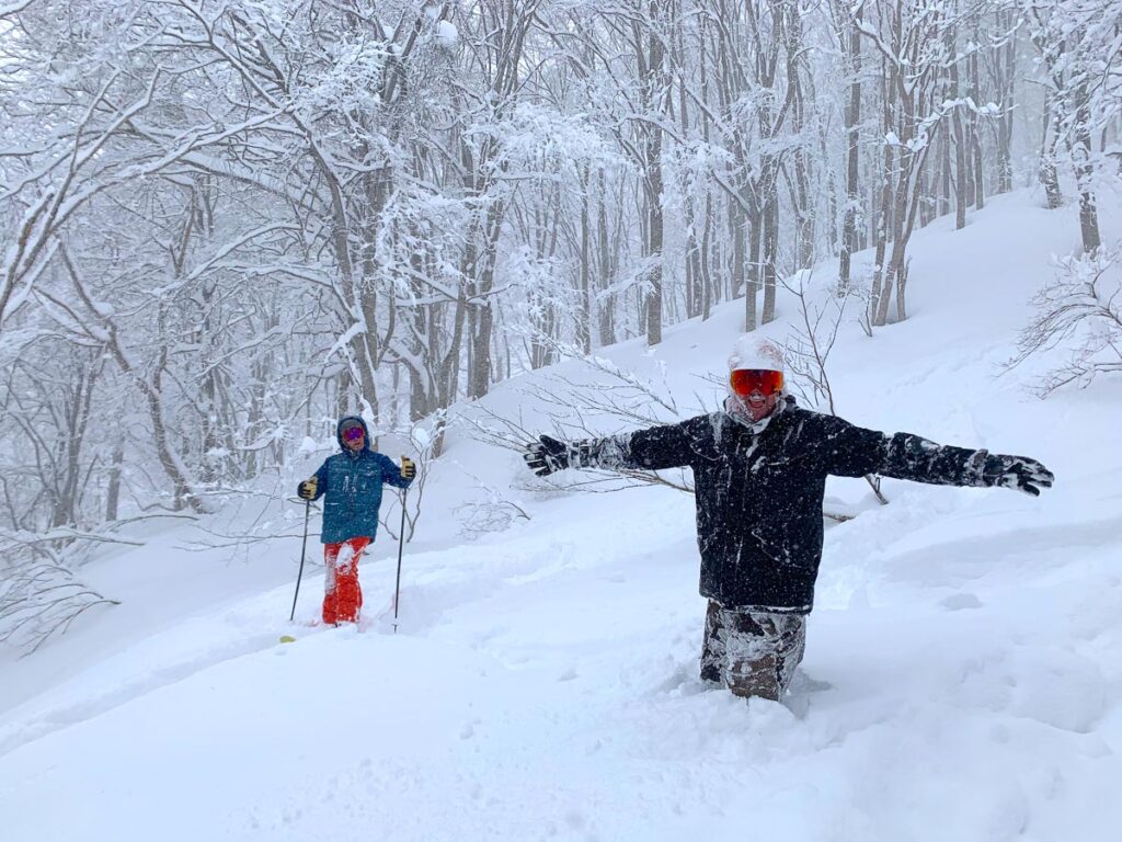 a skier and a snowboarder, thigh deep in fresh powder in the forest