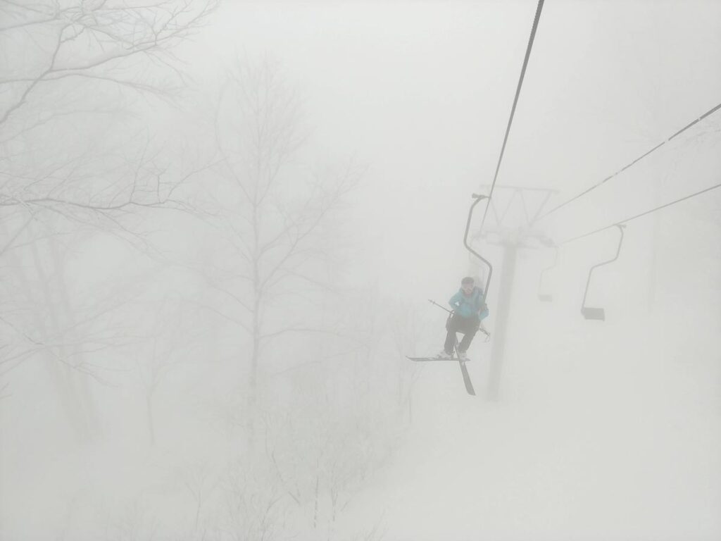 cloudy, white out and a single skier seen riding a single-seater chairlift