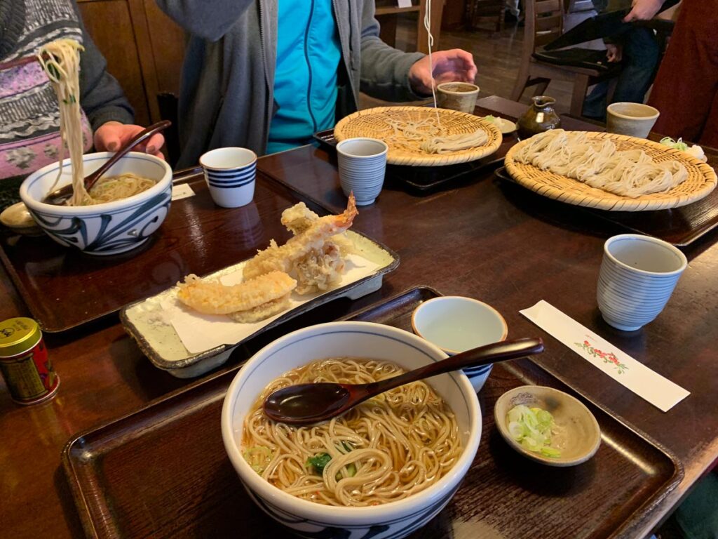 four plates of noodles, with some tempura prawns in the middle of the table