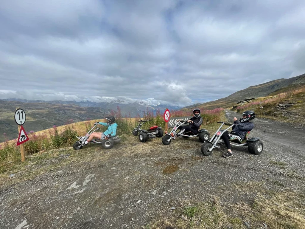 three adults wearing heavy duty helmets sitting on trike-like go carts in the high mountains