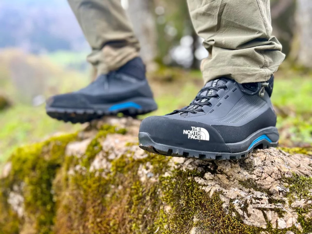 black hiking boots are pictured standing on a rock, the grassy background a blur