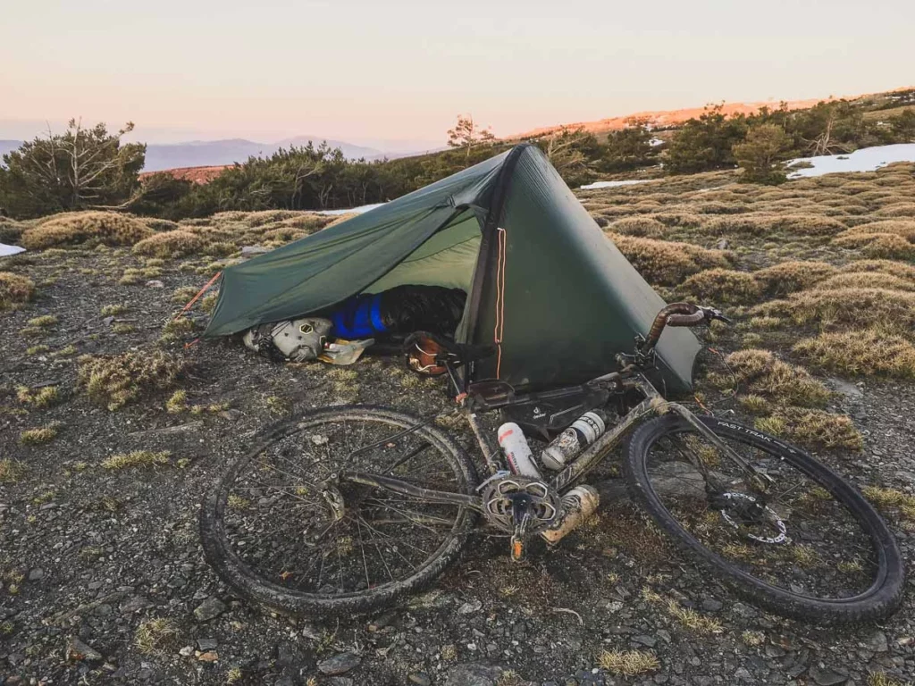 tent pitched, with bike lying on floor outside, ready for night. Little snow in the background