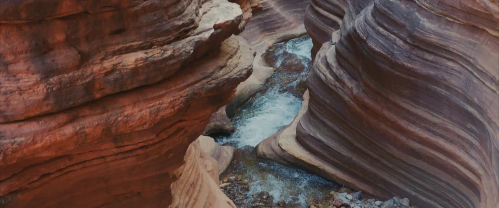 smooth rock (part of the Grand Canyon) is pictured with what looks like layers, from the water running through at the base of the canyon