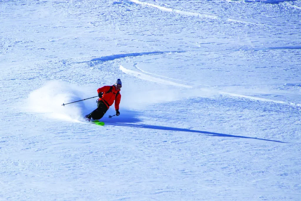 a telemark skier in red is pictured making a lovely smooth turn on fresh snow