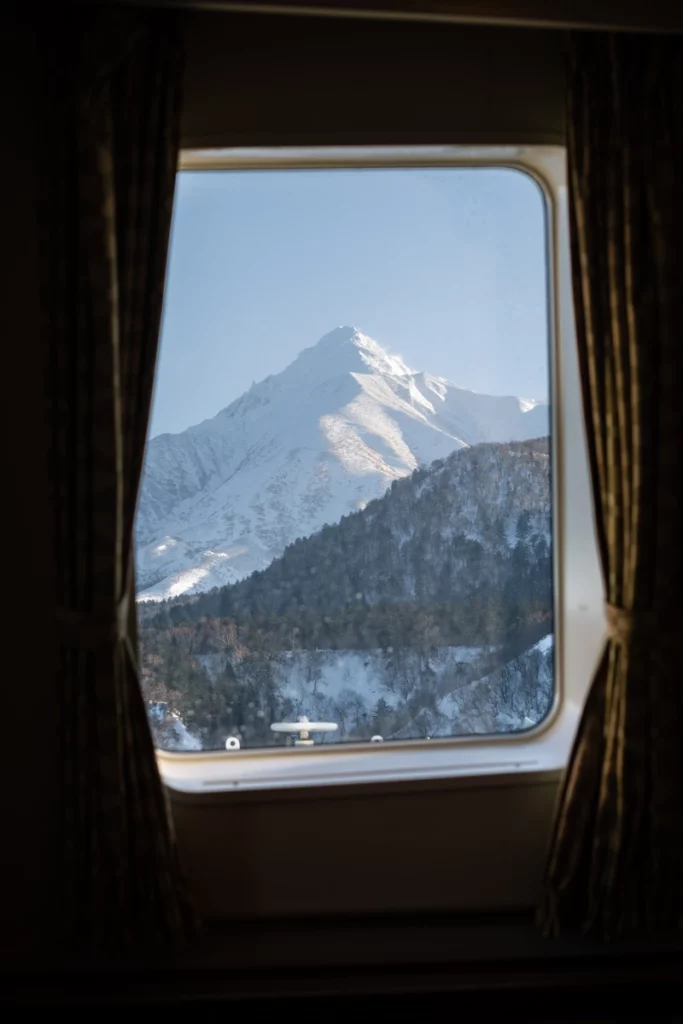 Mount Rishiri, white with snow, is framed and pictured through a curtained window of a ferry or train