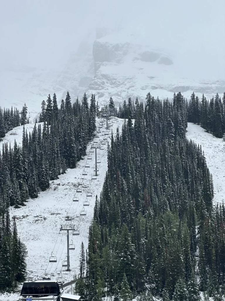 first snow covers a ski slope (cut into the alpine) with a ski lift visible on the central trail