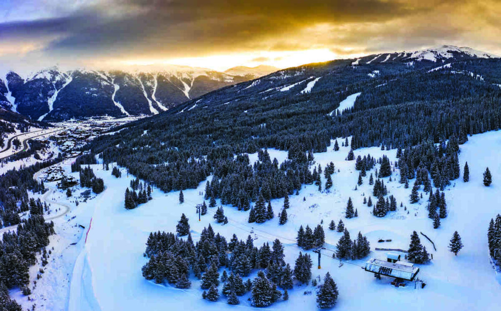 a yellow sunset over mountains covered in forest and snow