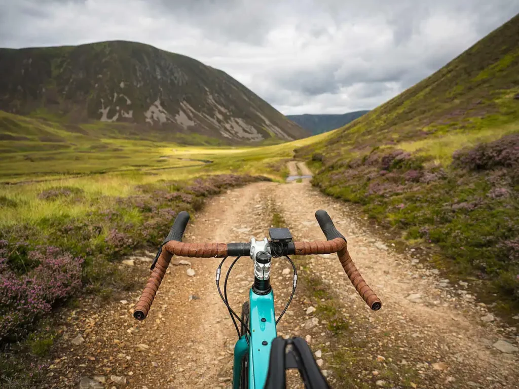 a bike's brown leather dropped handlebars are in shot as rider takes a picture over bike to green, Scottish landscape on a gravel trail