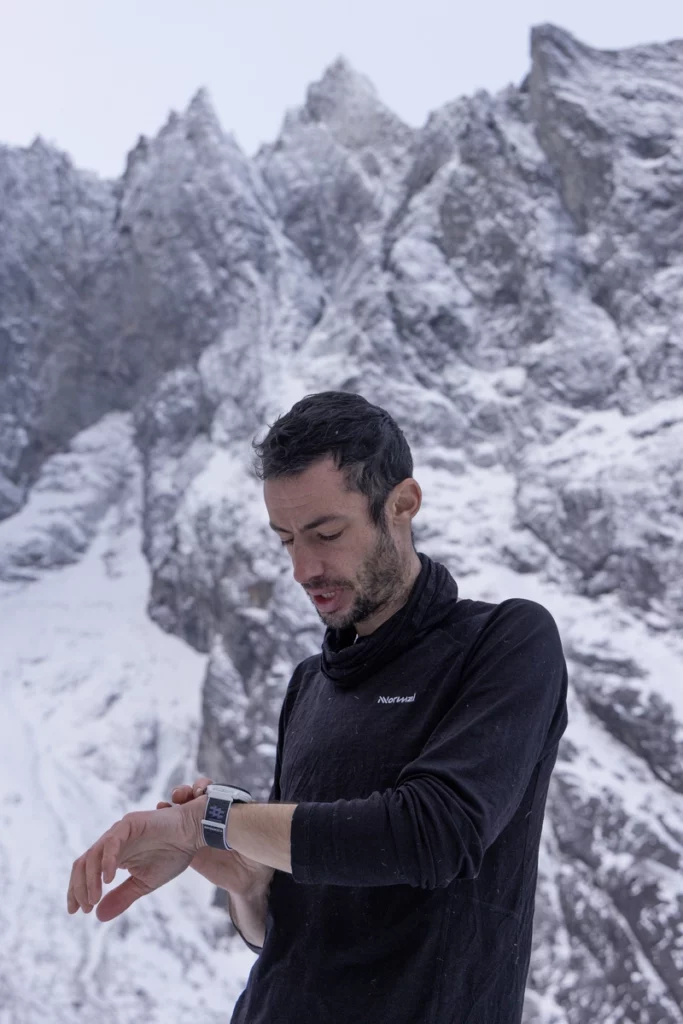 Ultra athlete Kilian Jornet checks his watch, in front of a blurred backdrop of a steep, snowy mountain face