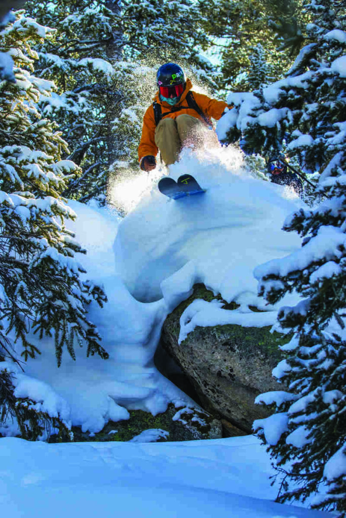 a skier pops off a snow topped rock