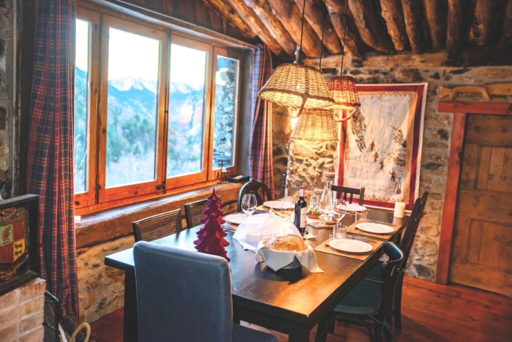 Andorra Dining Room with Mountain View: Cozy dining room with rustic decor and large windows showcasing the snowy Pyrenees mountains in Andorra.