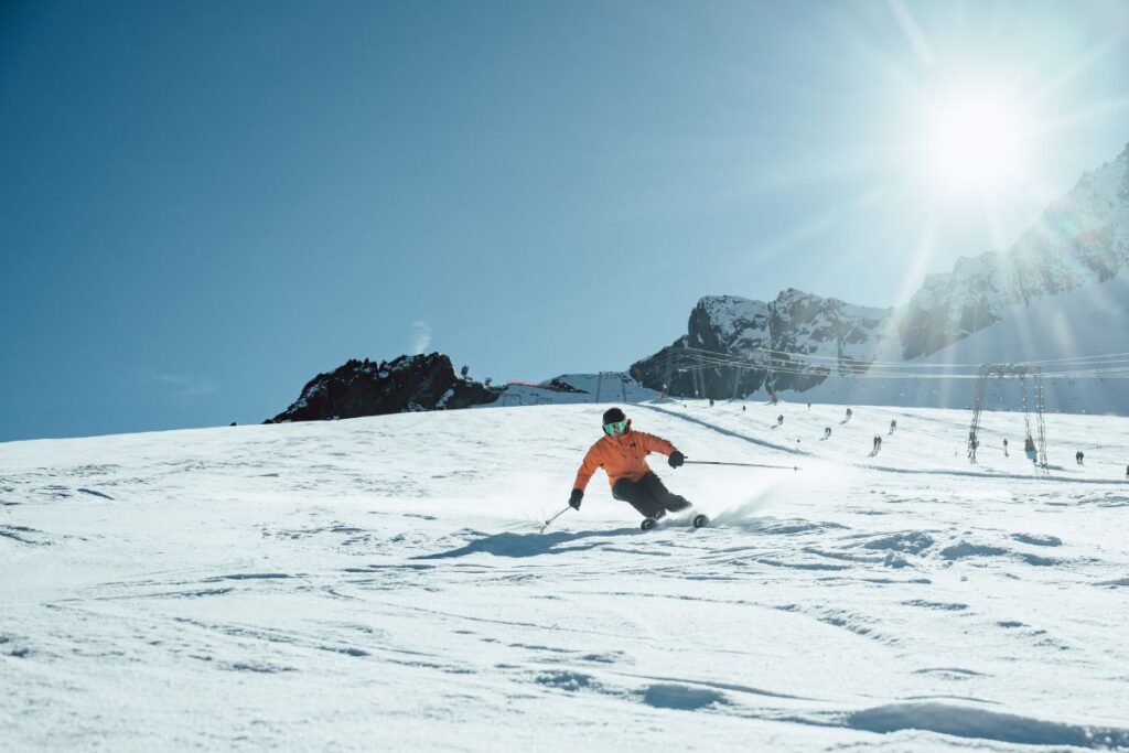 Skier in an orange jacket making smooth turns under a bright sunlit sky