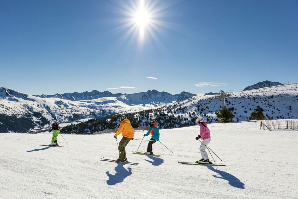 Skiers on Grandvalira’s Sunny Slopes: Skiers descending a sunny slope at Grandvalira resort, with breathtaking Pyrenees mountain scenery in the background.