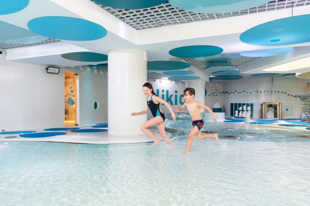 Children Playing in Andorra Spa Pool: Two children joyfully playing in a bright indoor spa pool with a modern blue-and-white design in Andorra.